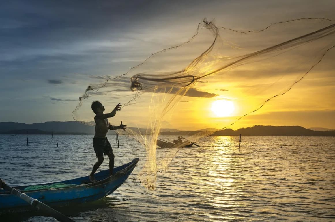 A fisher casting a net from a boat in golden evening light